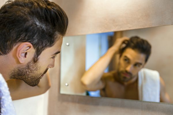 man examining receding hairline in mirror normal hair loss viviscal blog