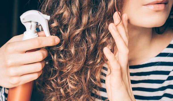Woman spray styling long brown curly hair top tips fixing dull hair Viviscal hair blog